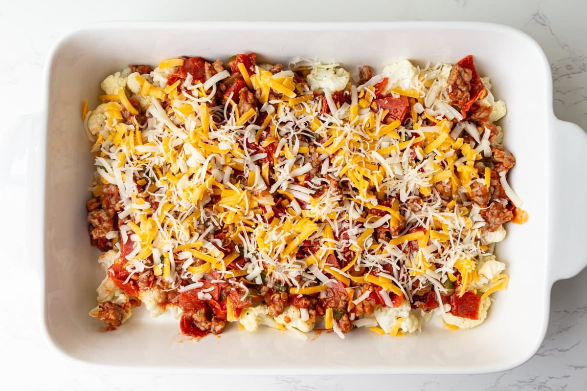 Baking dish layered with roasted cauliflower, sausage and marinara mixture, and shredded cheddar and mozzarella cheese.