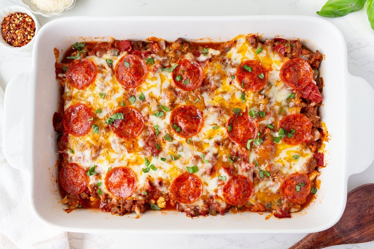 Baked keto pizza casserole with bubbly melted cheese, crispy pepperoni, and chopped basil on top.