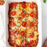 Overhead shot of keto pizza casserole in a white baking dish, topped with melted cheese, pepperoni, and fresh basil.