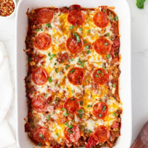 Overhead shot of keto pizza casserole in a white baking dish, topped with melted cheese, pepperoni, and fresh basil.