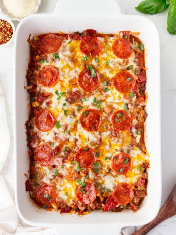Overhead shot of keto pizza casserole in a white baking dish, topped with melted cheese, pepperoni, and fresh basil.