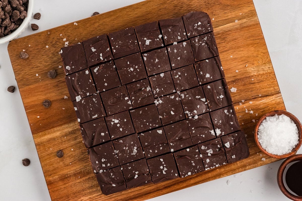 Gluten-free dairy-free chocolate fudge cut into 36 squares on a wood cutting board, sprinkled with flaky sea salt