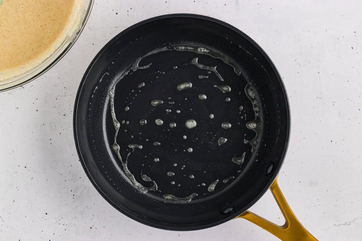 Melted butter coating a black skillet before cooking oat flour pancakes.