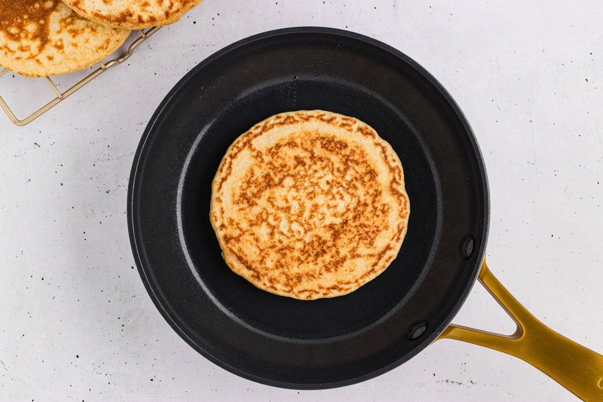 Oat flour pancake in a skillet with golden brown spots on the bottom.