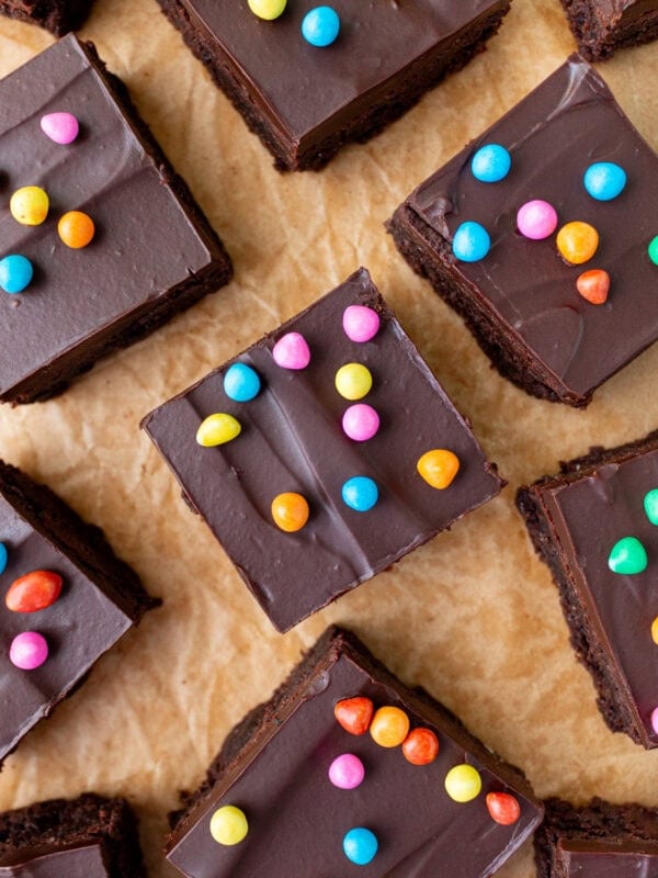 Overhead shot of gluten-free cosmic brownie squares topped with chocolate ganache and rainbow candy chips scattered on parchment paper.