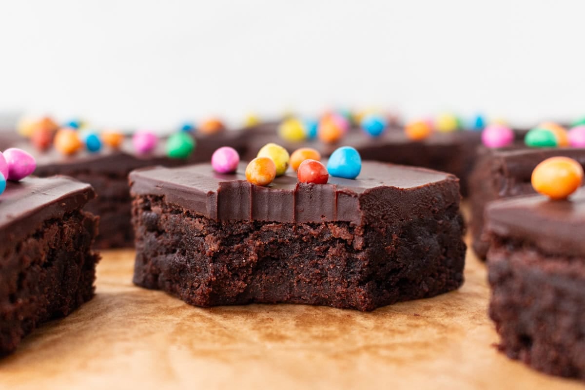 Close-up of a gluten-free cosmic brownie with a bite taken out, showing the fudgy interior and glossy ganache topping.