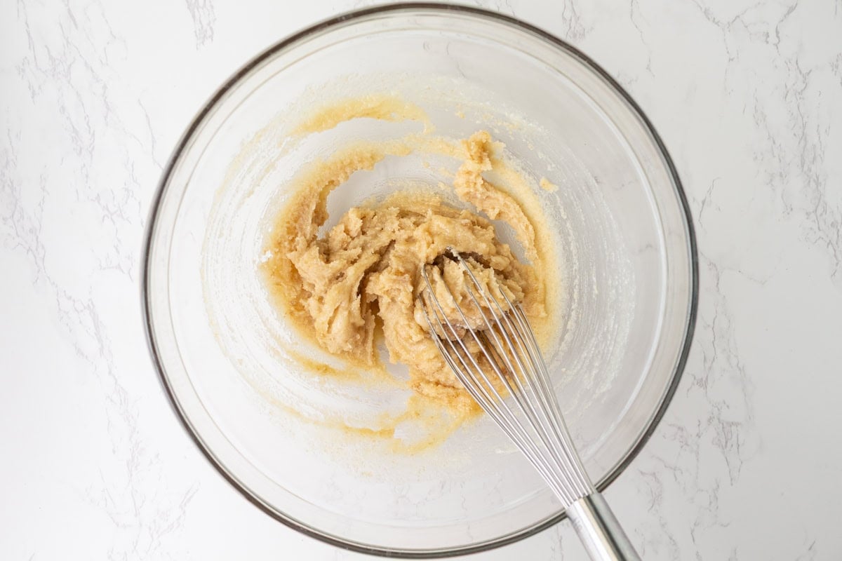 Melted butter whisked with granulated and brown sugar in a glass mixing bowl for gluten-free cosmic brownie batter.