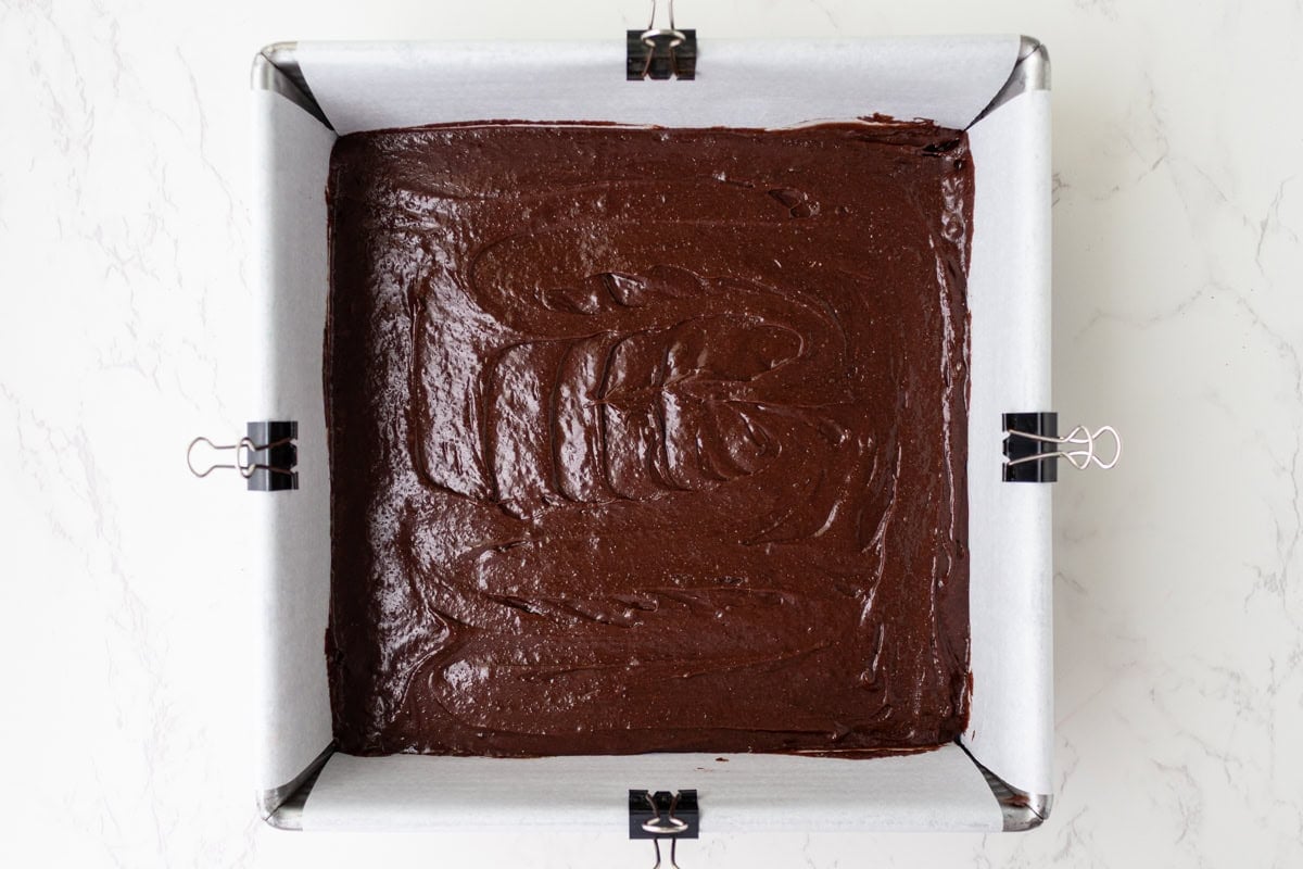 Gluten-free cosmic brownie batter spread into a parchment-lined 8x8 pan before baking.