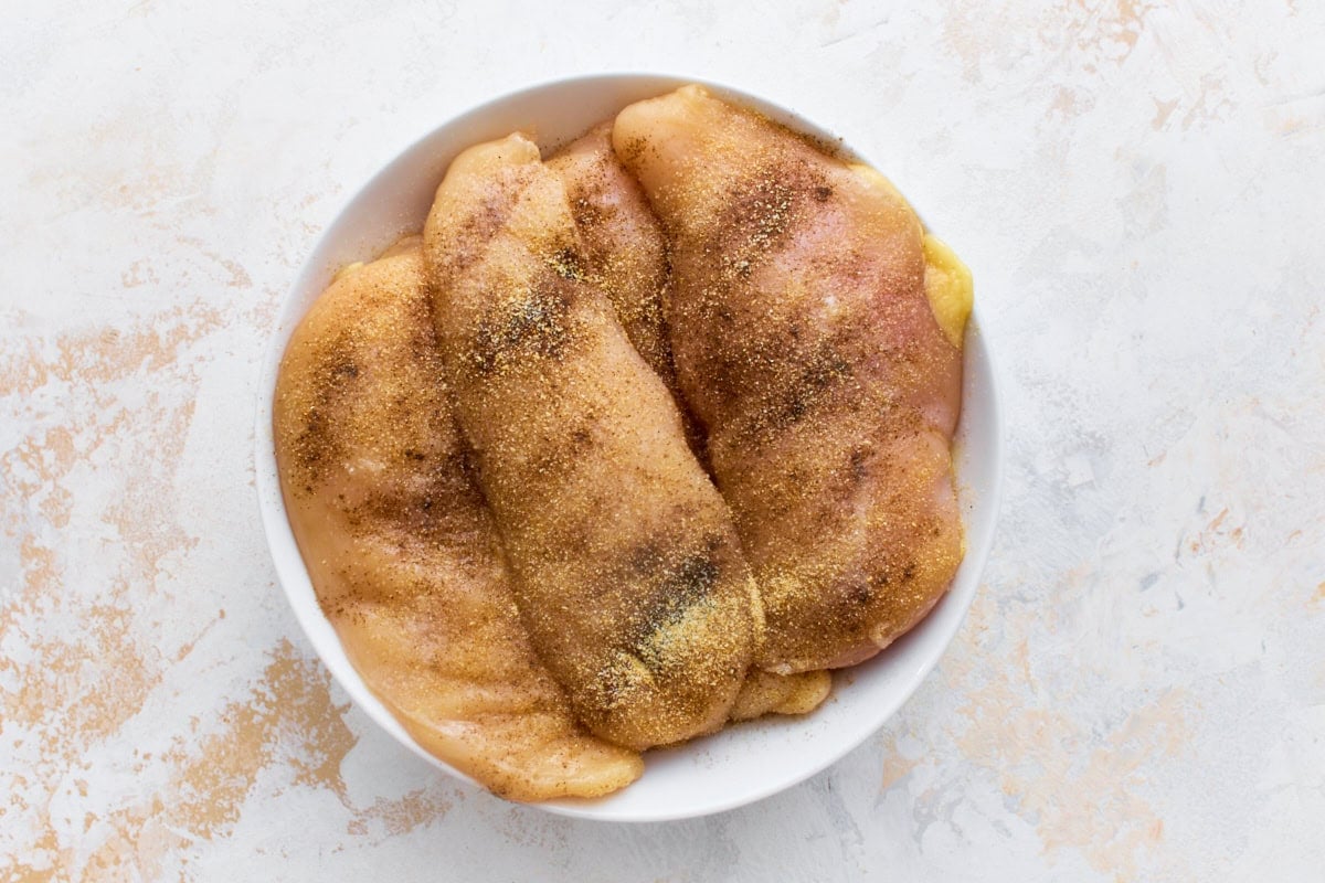 Raw chicken breasts seasoned with salt, pepper, and garlic powder in a white bowl, ready to sear for dairy-free Marry Me Chicken.