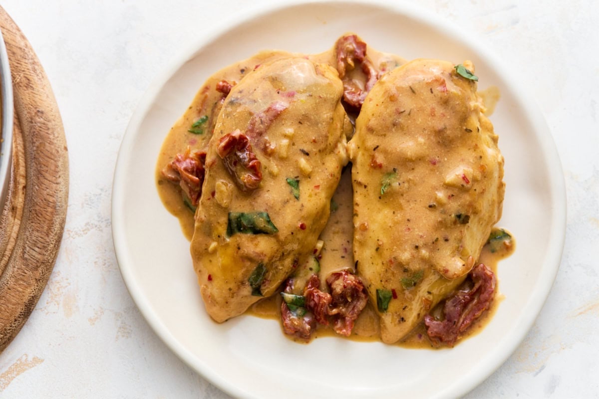 Two chicken breasts plated with creamy dairy-free Marry Me Chicken sauce, sun-dried tomatoes, and fresh basil.