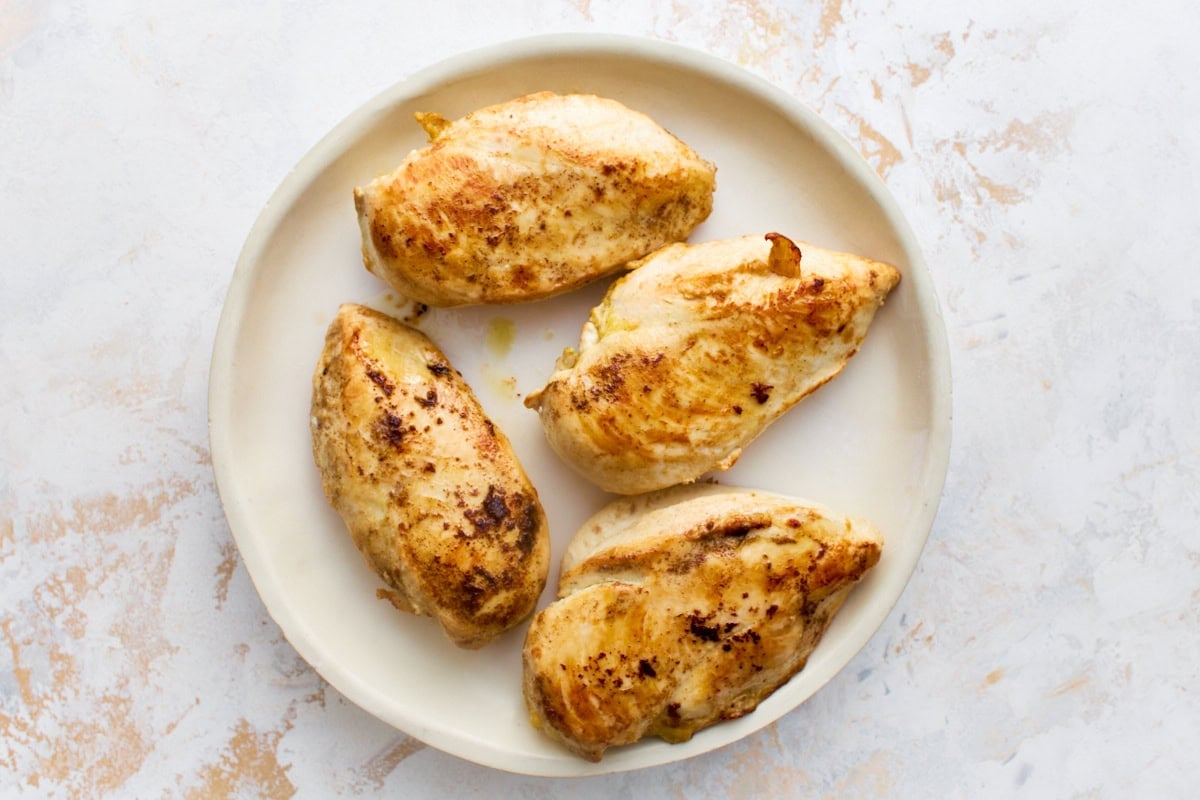 Four golden pan-seared chicken breasts resting on a plate before simmering in the dairy-free Marry Me Chicken sauce.