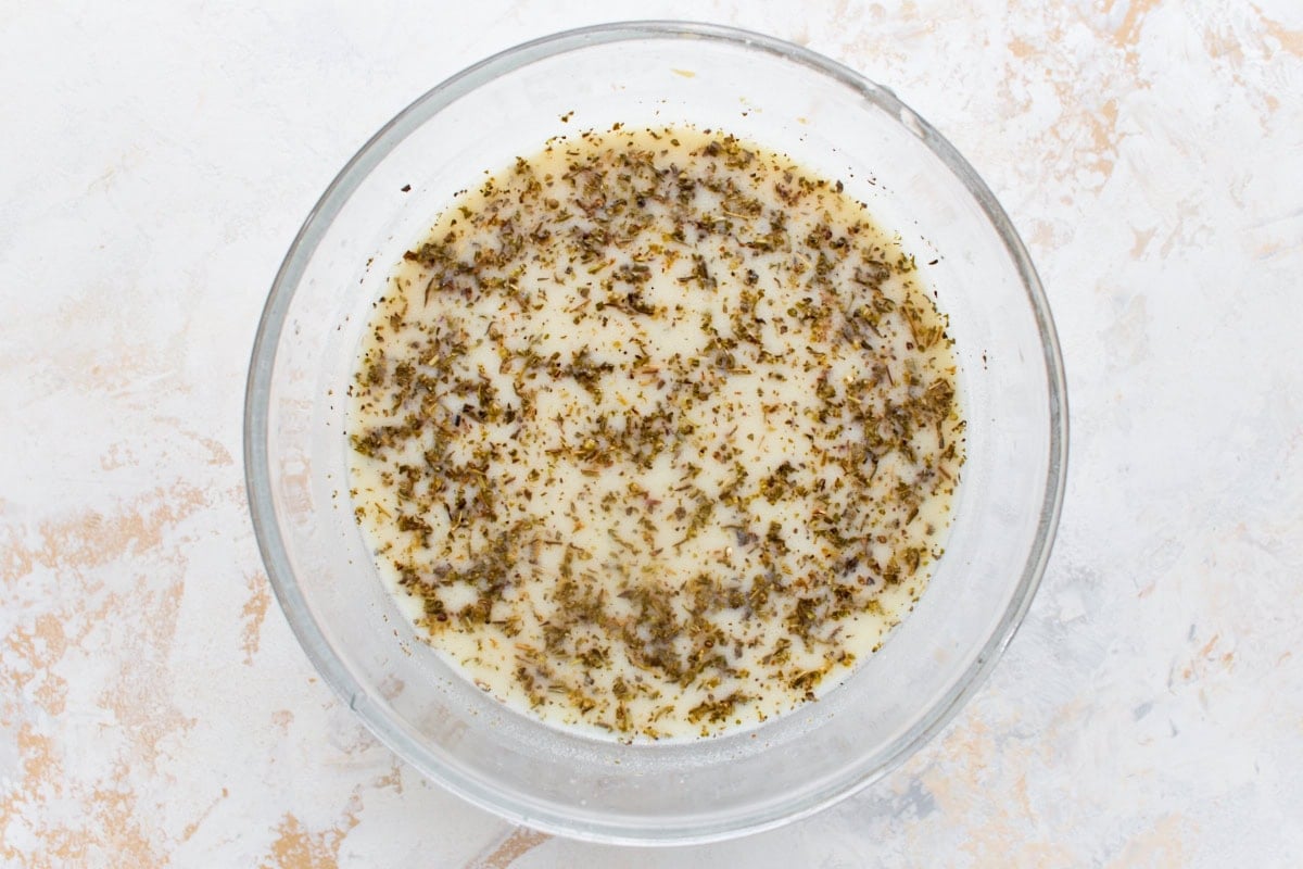 Chicken broth and coconut milk whisked together with nutritional yeast, cornstarch, and dried oregano in a glass bowl.