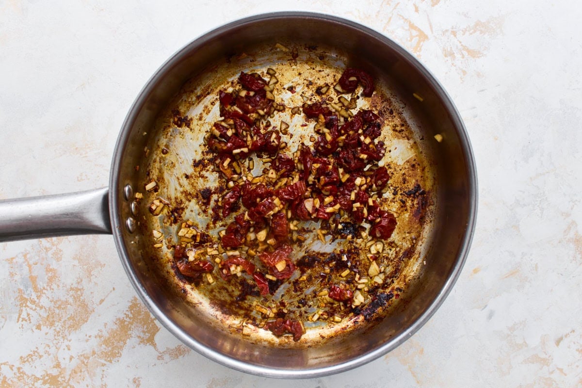 Minced garlic and chopped sun-dried tomatoes cooking in a skillet, the flavor base for dairy-free Marry Me Chicken sauce.