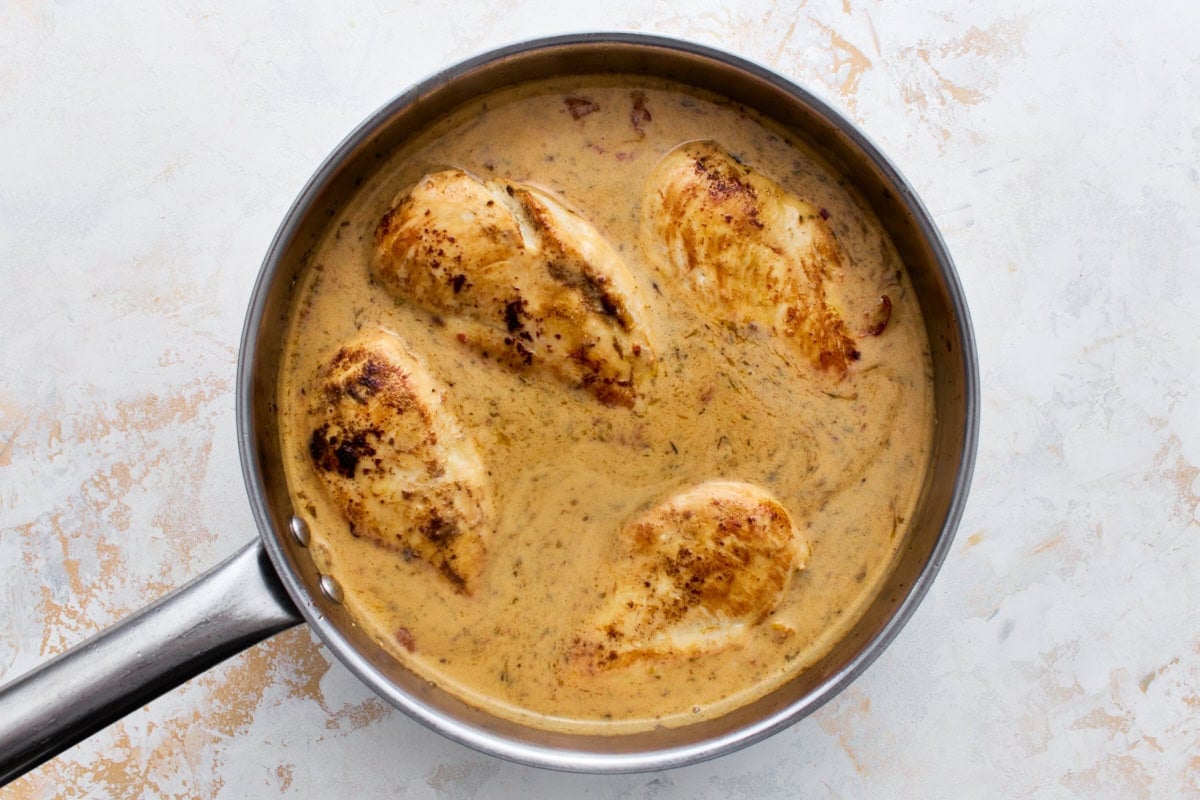 Seared chicken breasts nestled into the creamy sun-dried tomato sauce in a skillet, ready to cover and simmer.