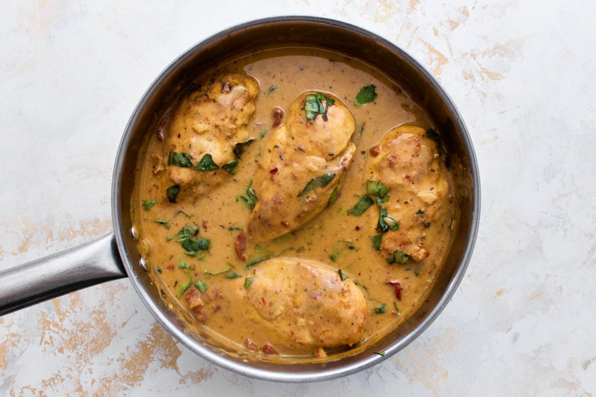 Overhead close-up of dairy-free Marry Me Chicken in a skillet, coated in a creamy sun-dried tomato sauce and topped with fresh basil.