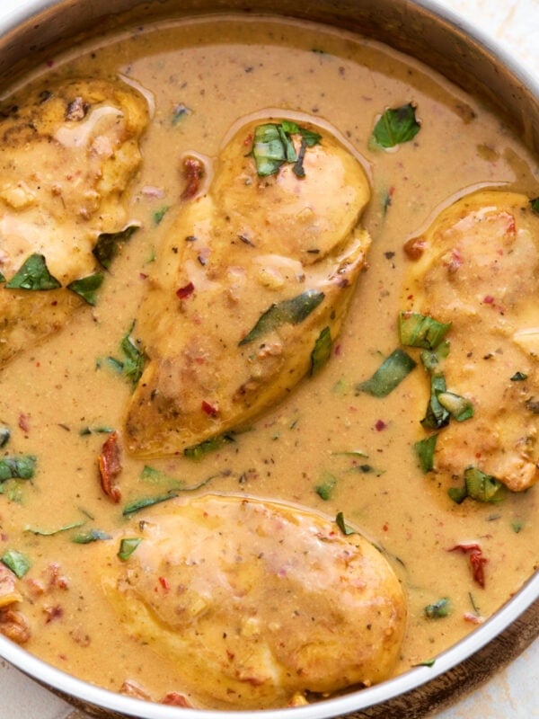 Overhead close-up of dairy-free Marry Me Chicken in a skillet, coated in a creamy sun-dried tomato sauce and topped with fresh basil.