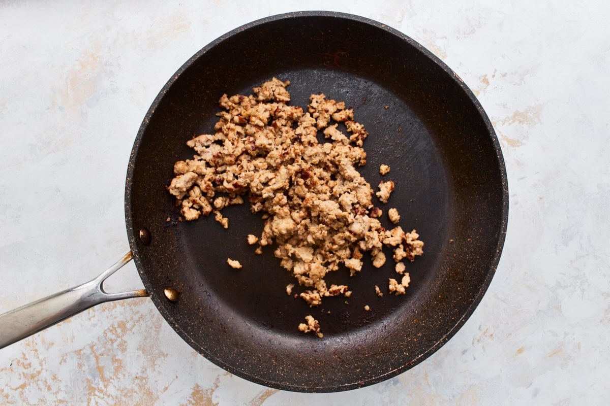 Browned breakfast sausage crumbles cooking in a nonstick skillet