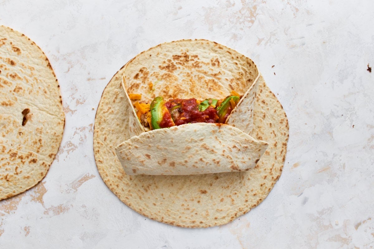 Gluten-free tortilla folded over breakfast burrito filling, showing how to roll it tightly