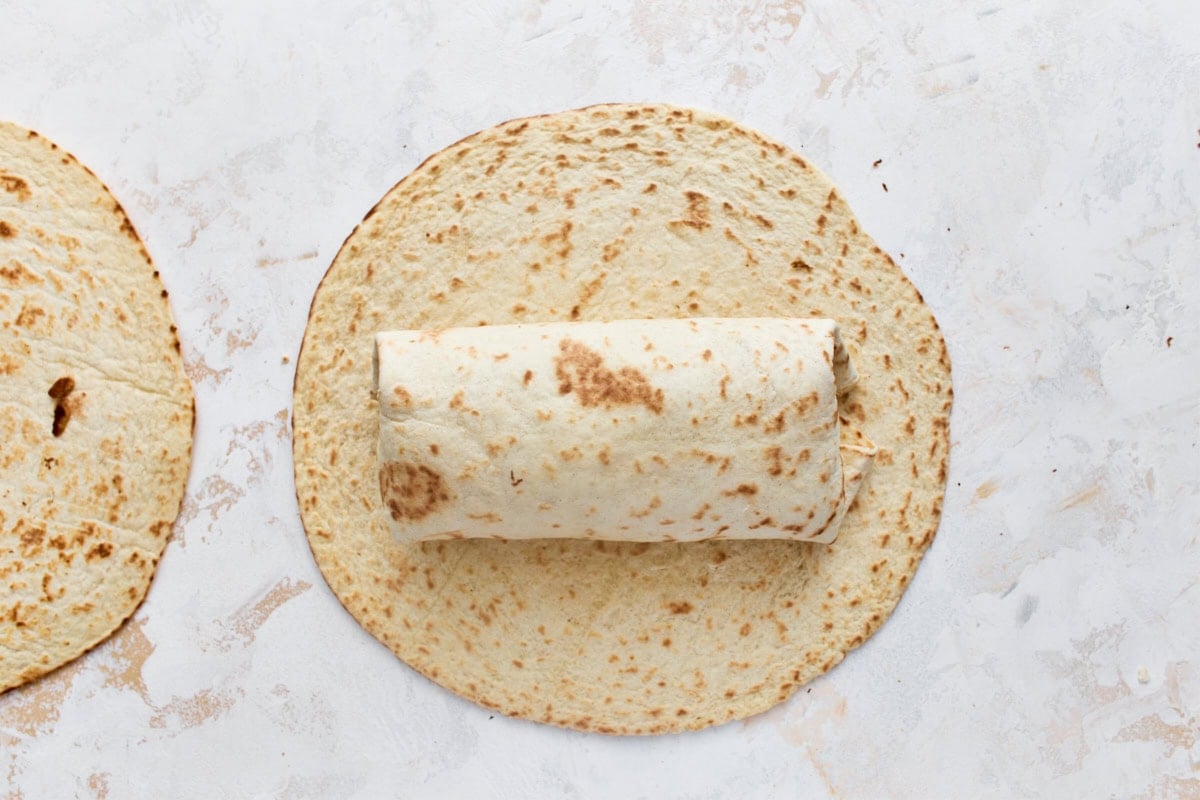 Rolled gluten-free breakfast burrito on a tortilla, ready to slice