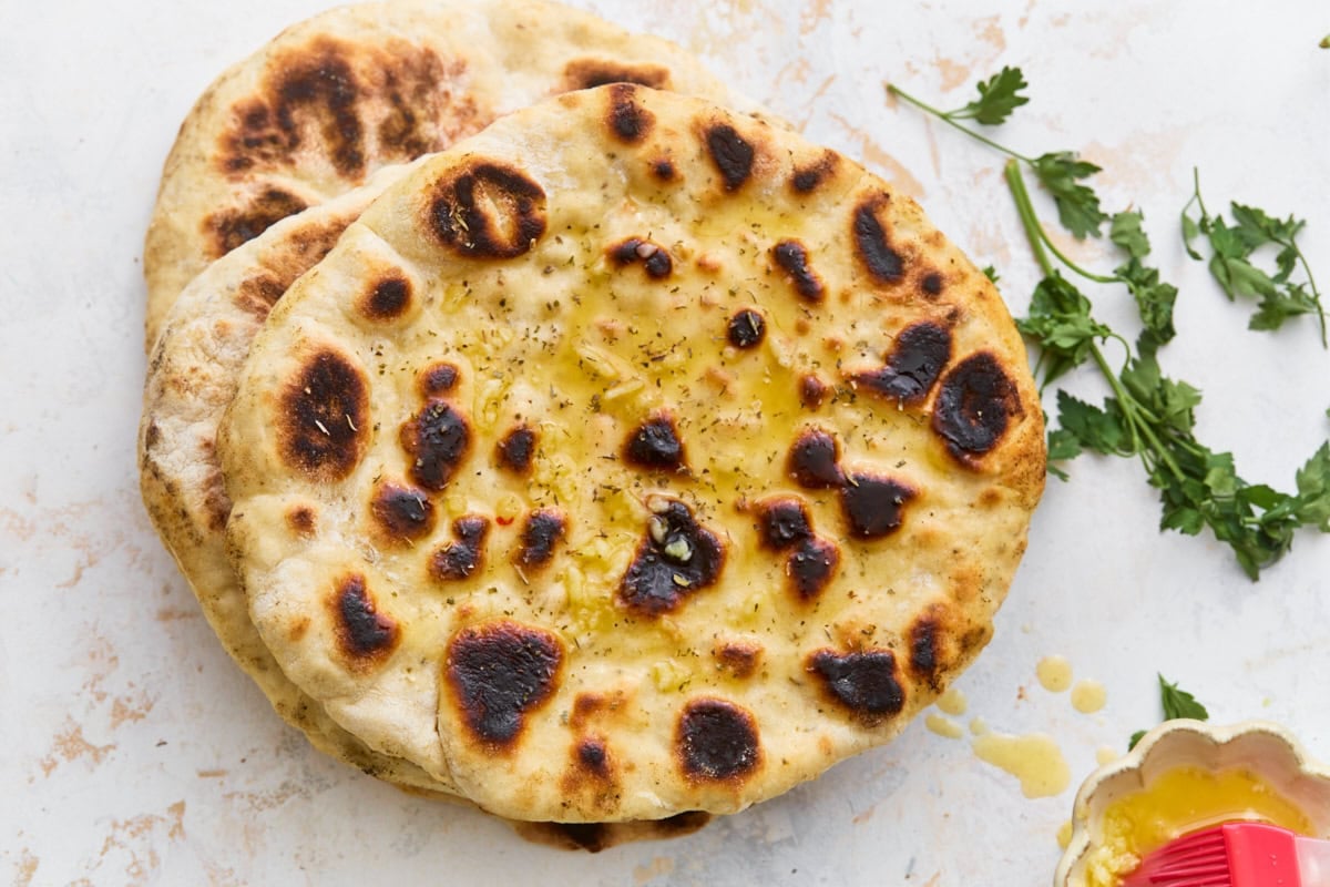 Stack of cooked gluten-free flatbreads brushed with melted butter and garlic, garnished with fresh parsley.