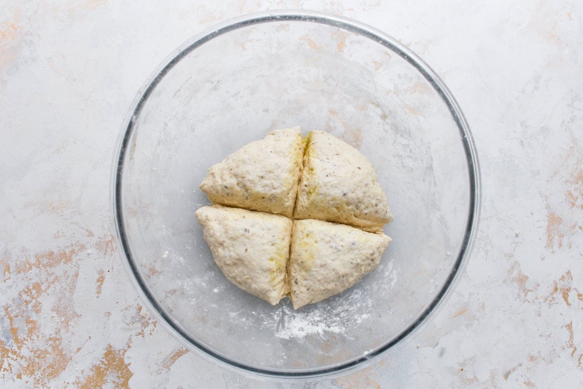 Gluten-free flatbread dough divided into four equal pieces in a glass mixing bowl.