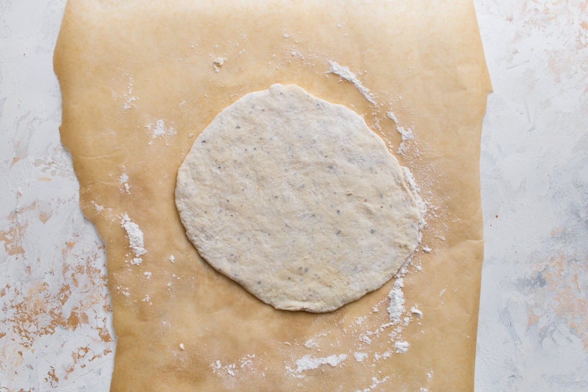 A piece of gluten-free flatbread dough rolled into a round on parchment paper.