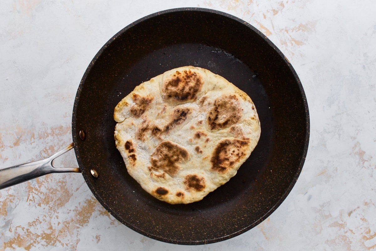 Gluten-free flatbread cooking in a nonstick skillet with golden-brown spots forming.
