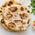 Two golden-brown gluten-free flatbreads stacked on a marble surface with fresh parsley alongside.