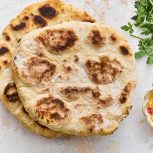 Two golden-brown gluten-free flatbreads stacked on a marble surface with fresh parsley alongside.