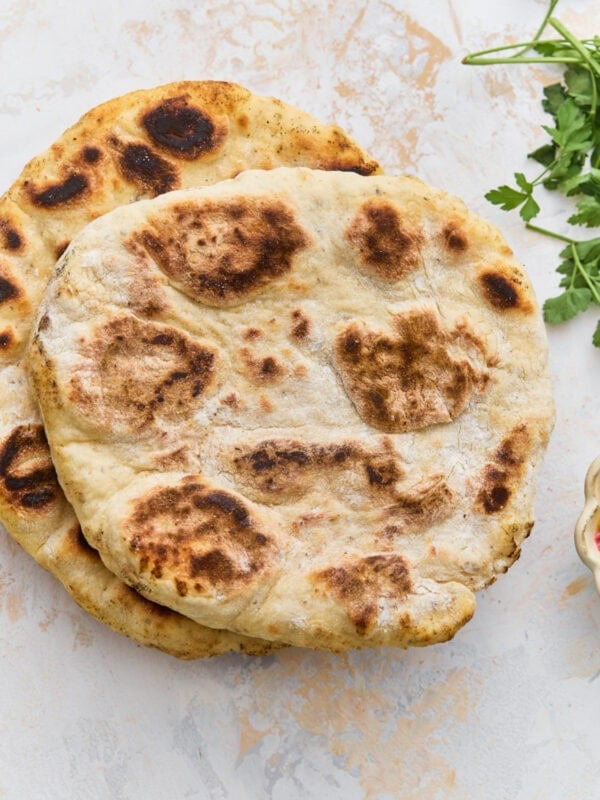 Two golden-brown gluten-free flatbreads stacked on a marble surface with fresh parsley alongside.