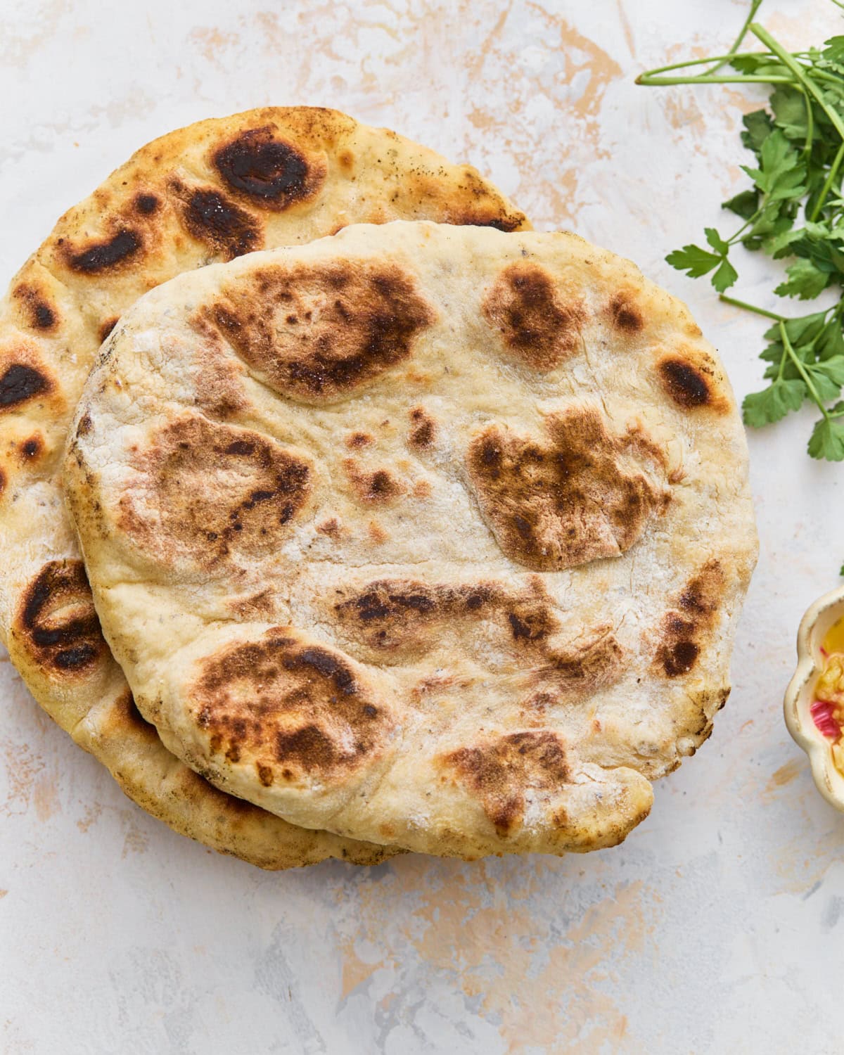 Two golden-brown gluten-free flatbreads stacked on a marble surface with fresh parsley alongside.