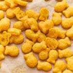 Gluten-free goldfish crackers scattered on parchment paper, with a few broken open to show the light, airy texture inside.