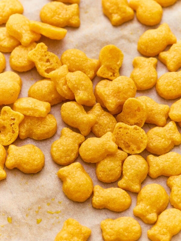 Gluten-free goldfish crackers scattered on parchment paper, with a few broken open to show the light, airy texture inside.