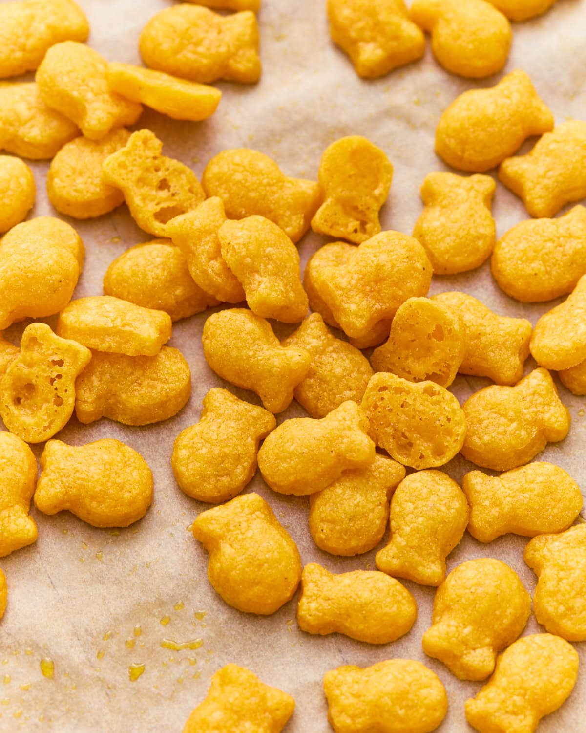 Gluten-free goldfish crackers scattered on parchment paper, with a few broken open to show the light, airy texture inside.