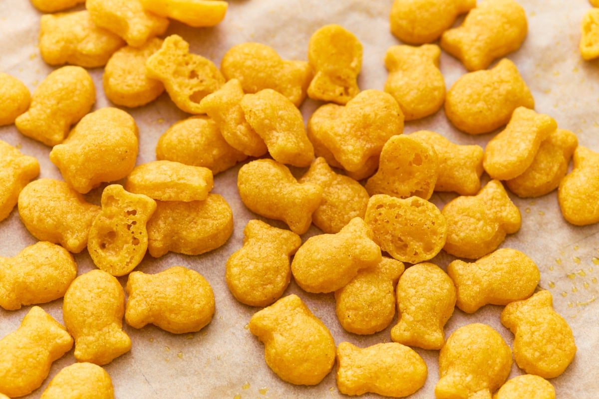 A close-up pile of golden, crispy gluten-free goldfish crackers on parchment paper.