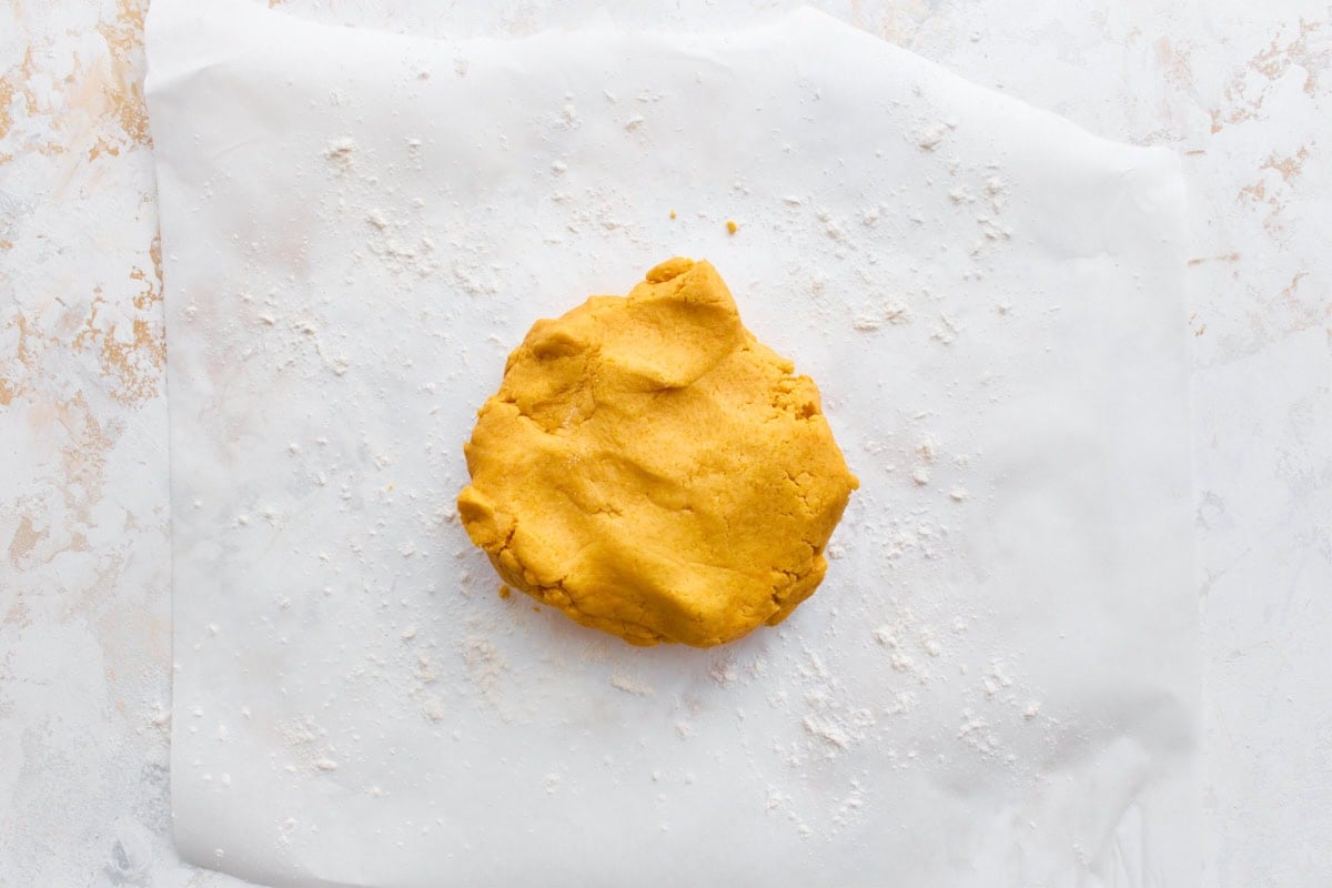 Gluten-free cracker dough pressed into a flat disk on parchment paper, ready to roll out.