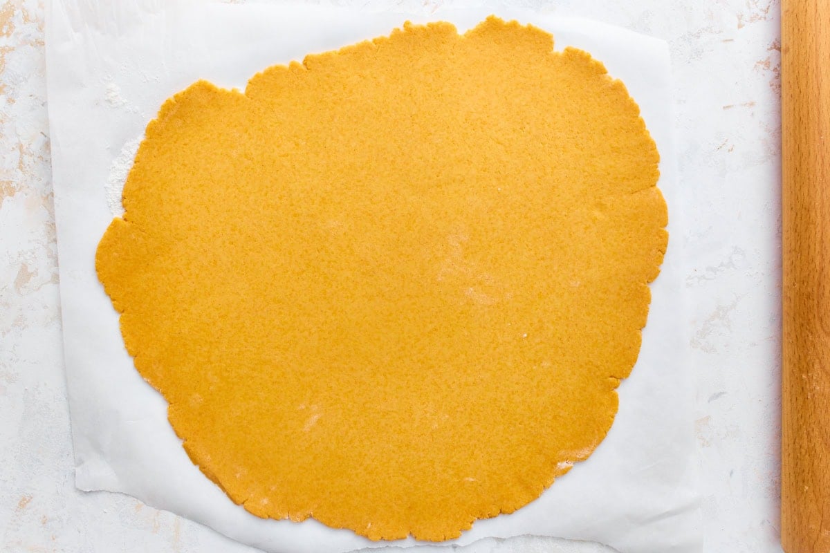 Gluten-free goldfish cracker dough rolled thin on parchment paper with a rolling pin.