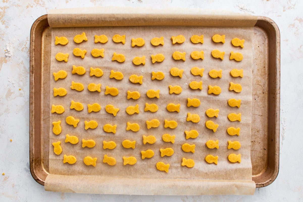 Rows of unbaked gluten-free goldfish crackers cut into fish shapes on a parchment-lined baking sheet.