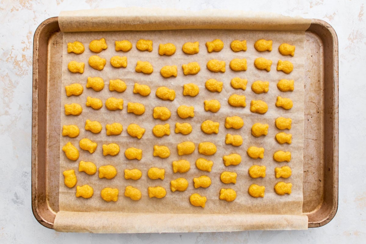 Rows of baked gluten-free goldfish crackers on a parchment-lined baking sheet, golden and crisp.