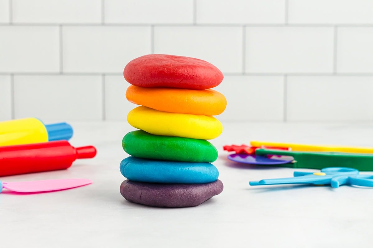 six colorful dough discs stacked together with play doh tools in the background