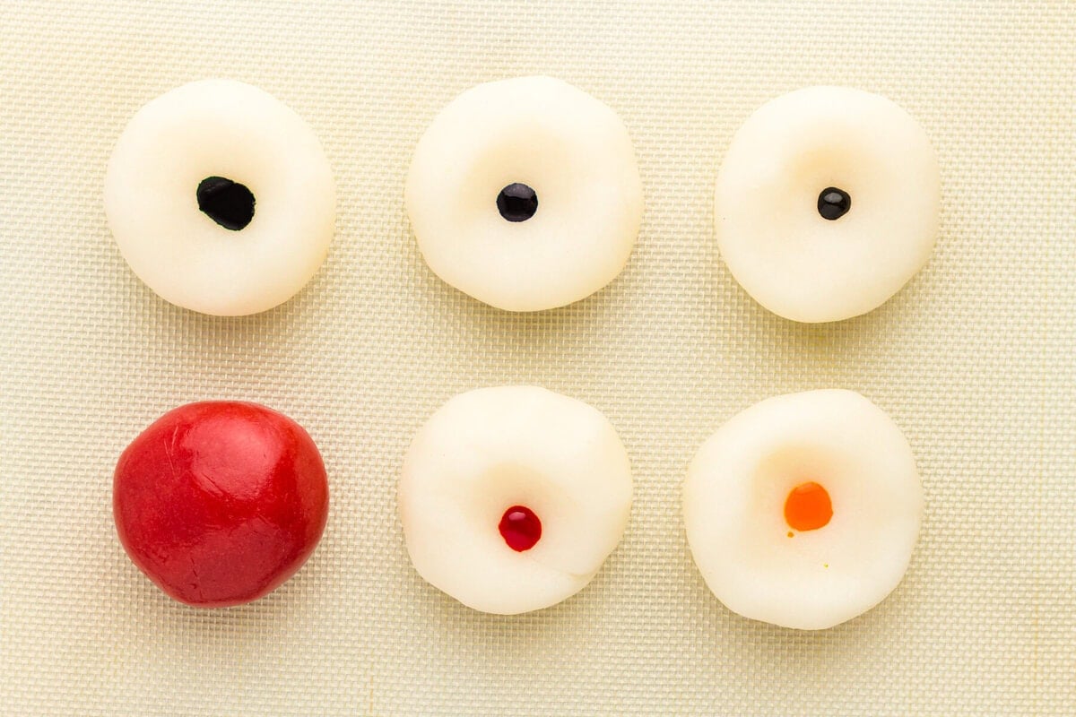 six white dough rounds, each with a drop of gel food coloring in the center before kneading