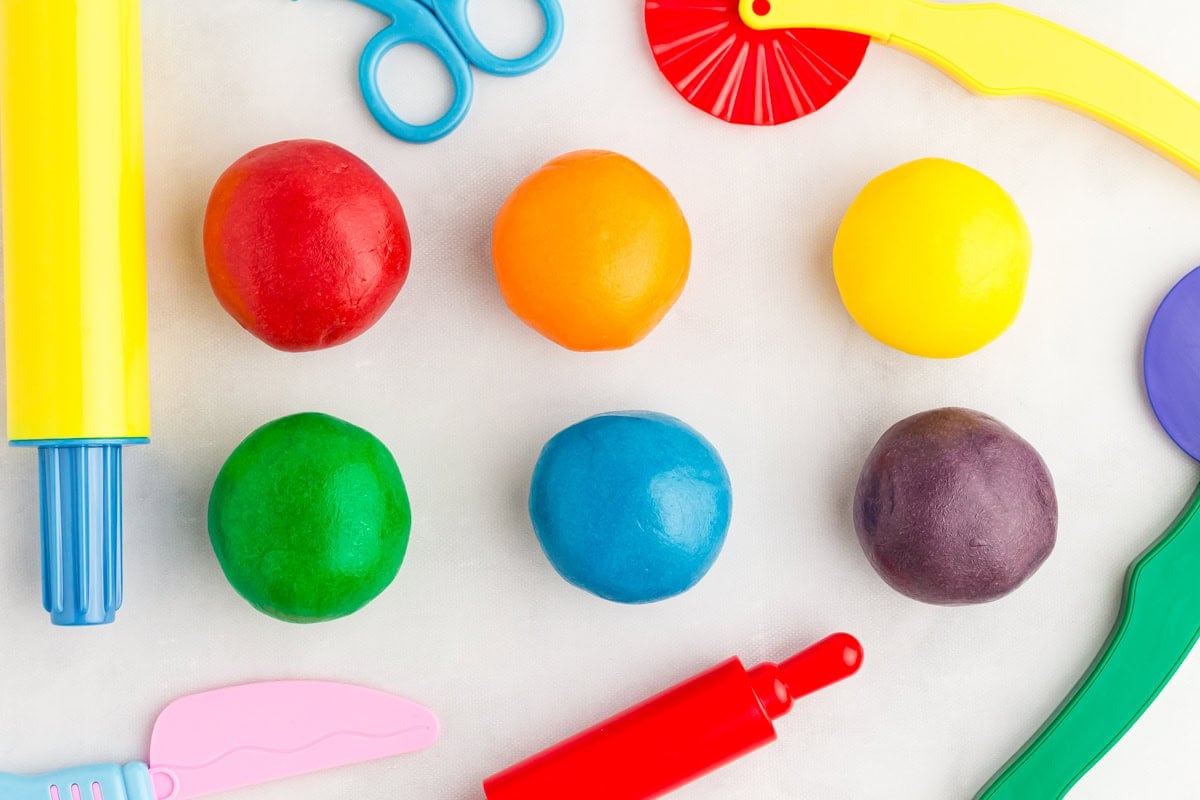 fully kneaded red, orange, yellow, green, blue, and purple play doh surrounded by kids' plastic play tools