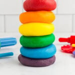 red, orange, yellow, green, blue, and purple play doh stacked on a kitchen counter