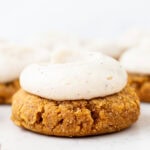 Gluten-free almond flour pumpkin cookie topped with brown butter cream cheese frosting, with more frosted cookies blurred in the background.