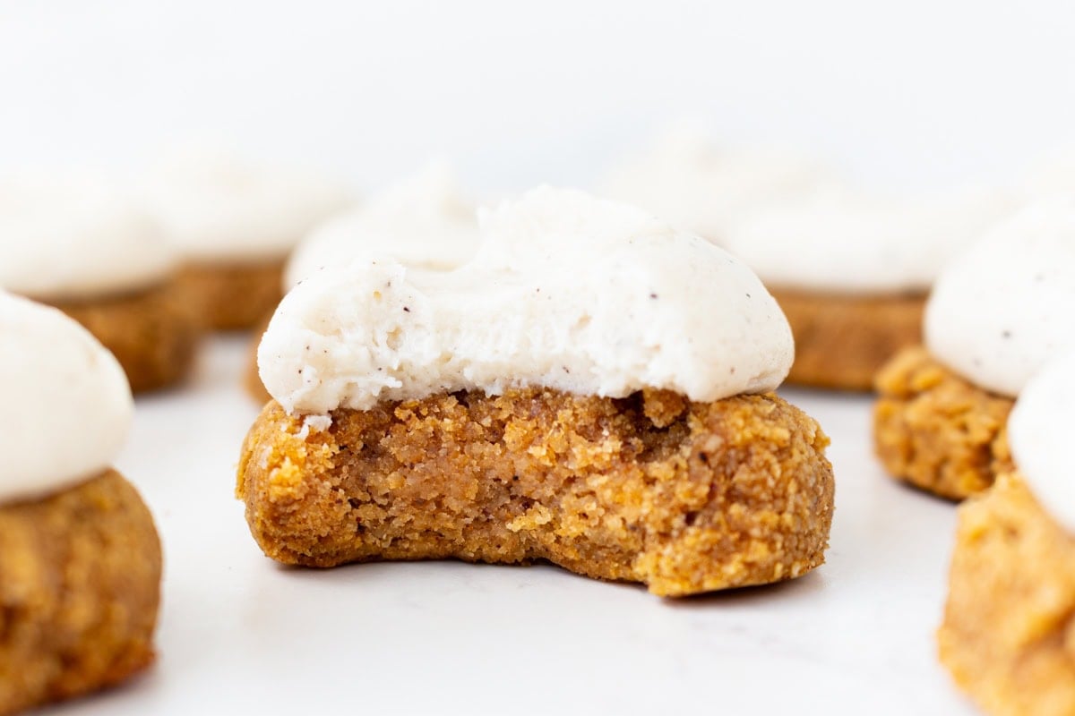 Close-up of a gluten-free almond flour pumpkin cookie with a bite taken out, showing the soft, cake-like texture inside.