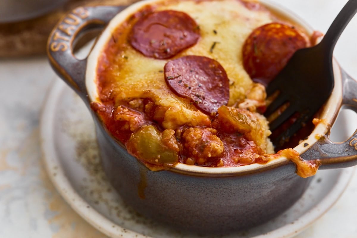 A fork lifting a bite of gluten-free crustless pizza bowl, showing melted cheese and sausage filling.