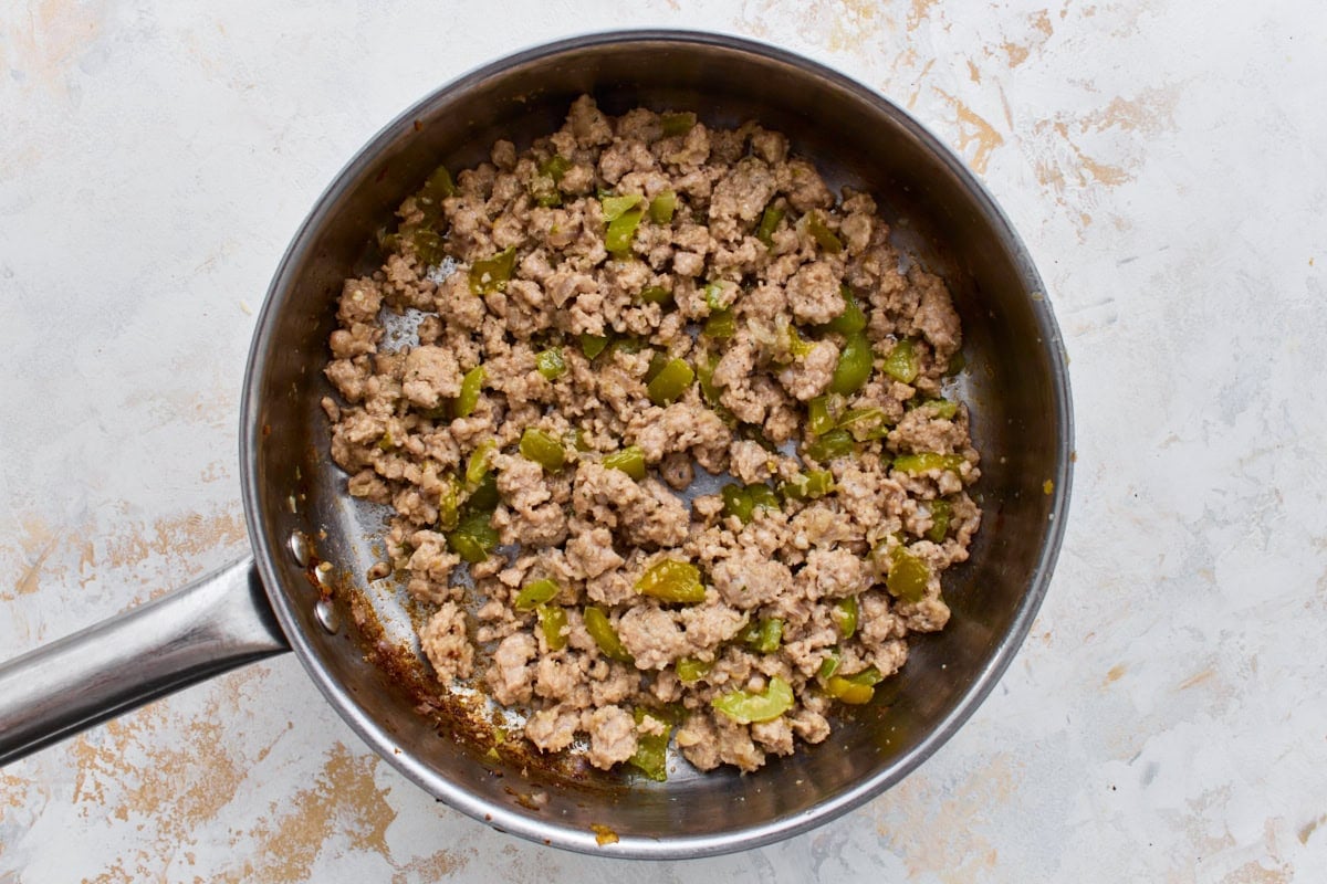 Browned Italian sausage and green bell pepper cooking in a skillet.