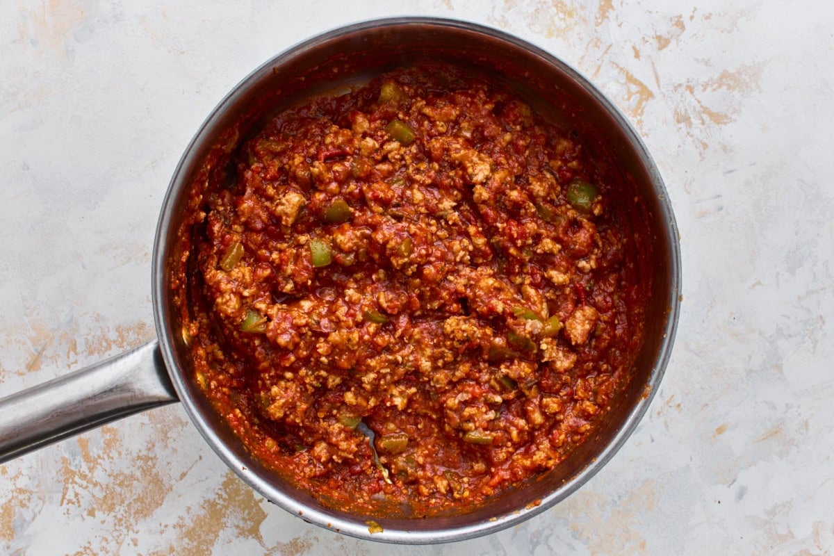 Italian sausage simmering in marinara sauce with Italian herbs in a skillet.