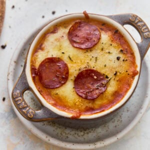 Overhead view of a gluten-free crustless pizza bowl with melted mozzarella, Parmesan, and pepperoni in a mini cast iron cocotte.
