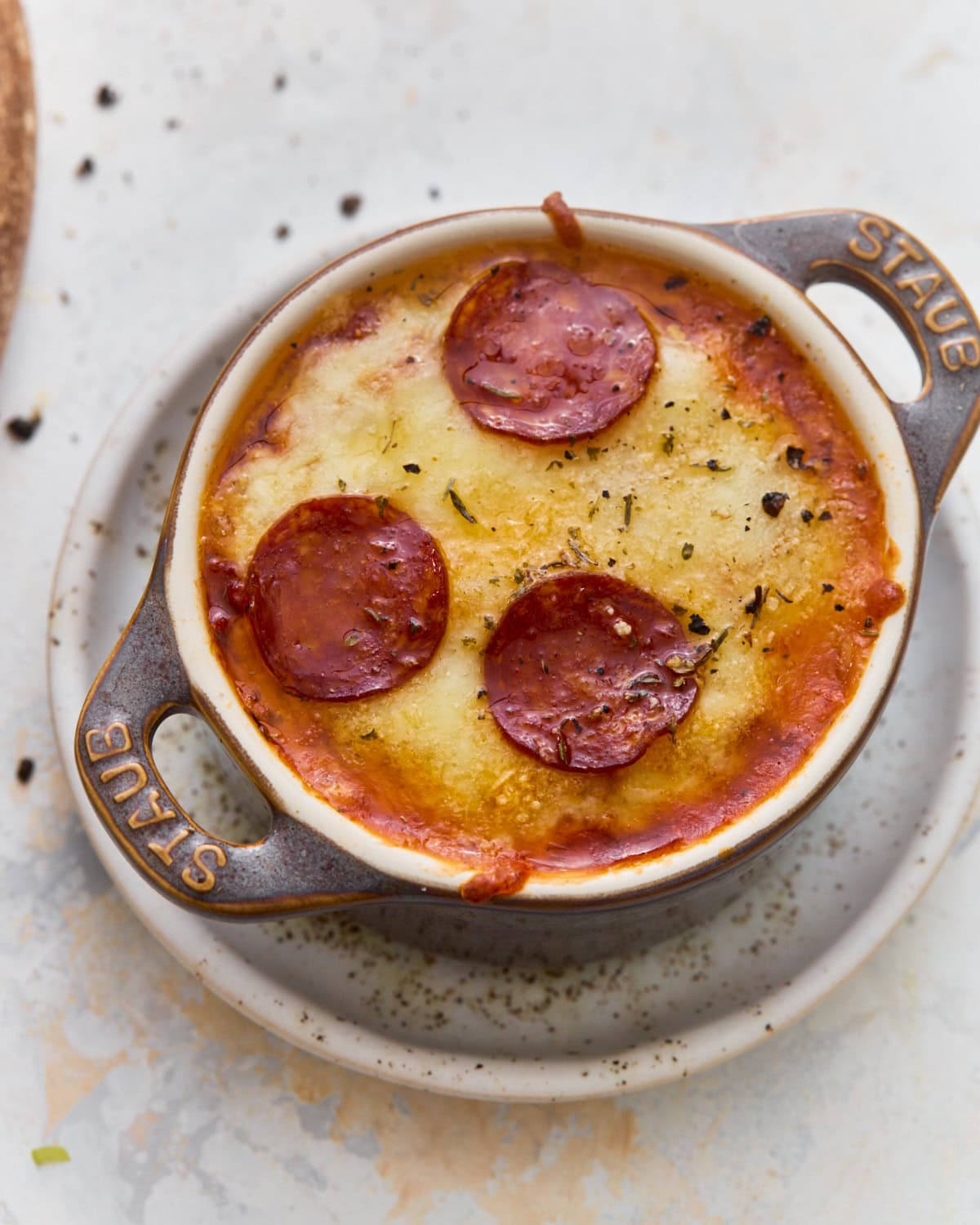 Overhead view of a gluten-free crustless pizza bowl with melted mozzarella, Parmesan, and pepperoni in a mini cast iron cocotte.